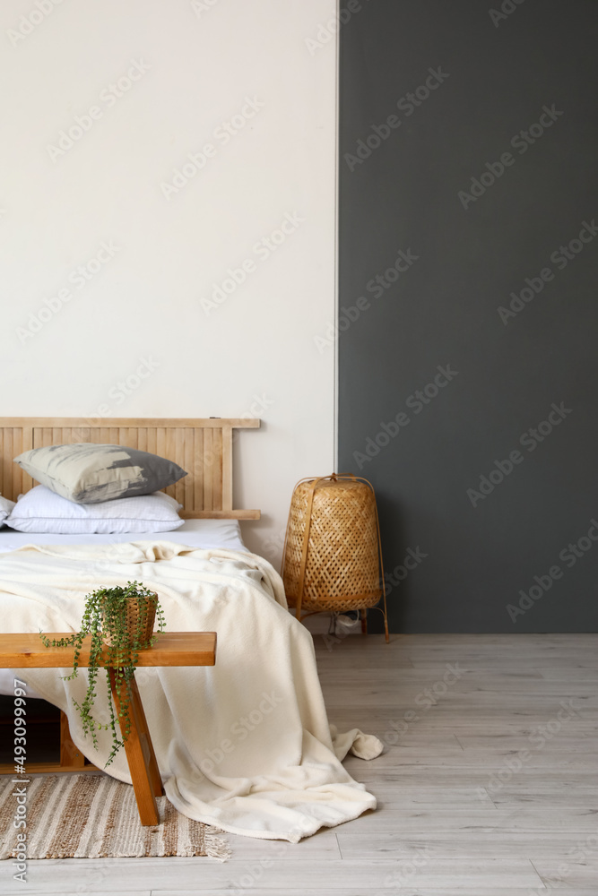 Wooden bench with houseplant, comfortable bed, lamp near black and white wall