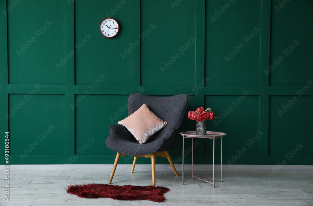 Vase with red peony flowers on coffee table and armchair near green wall