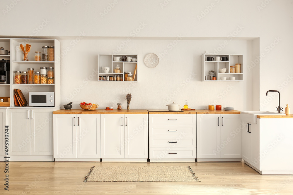 Interior of light modern kitchen with white counters, shelves and food