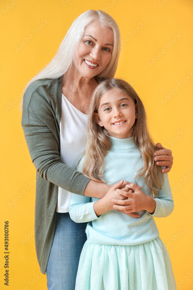 Mature woman hugging her little granddaughter on yellow background