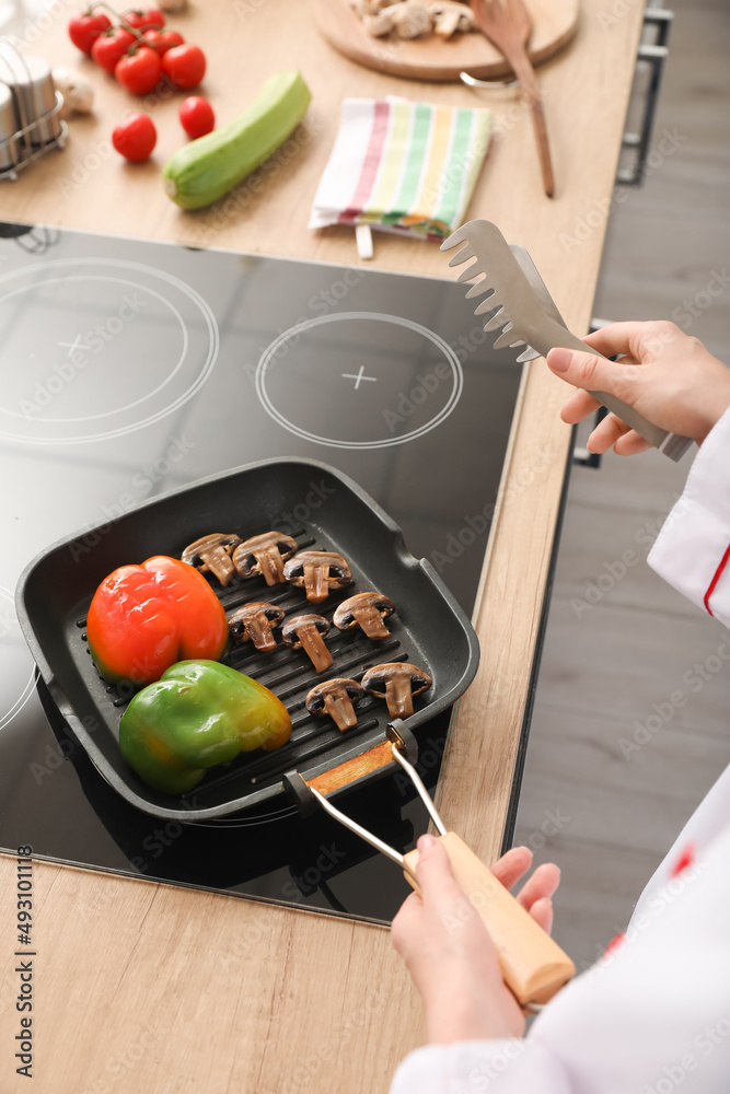 Female chef with tongs frying tasty vegetables in kitchen, closeup