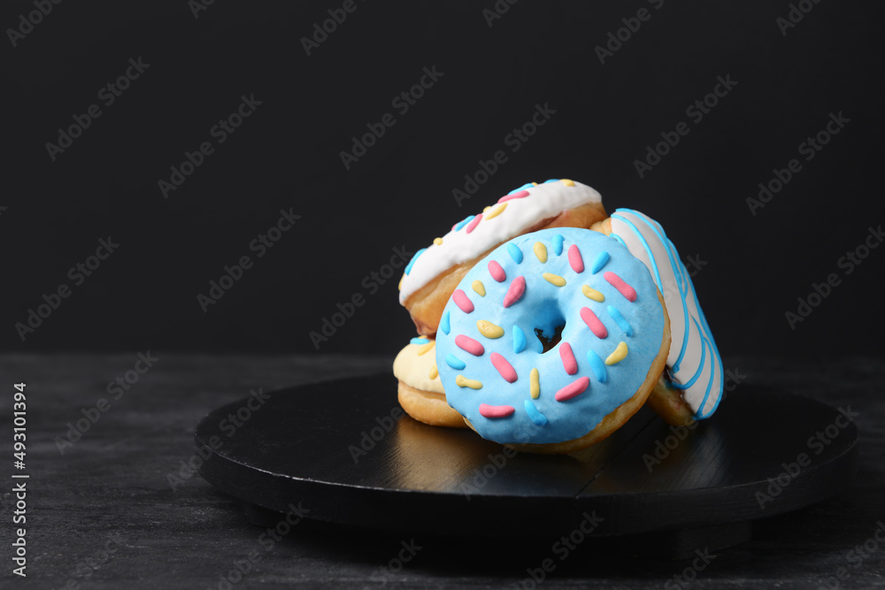 Board with delicious donuts on dark background