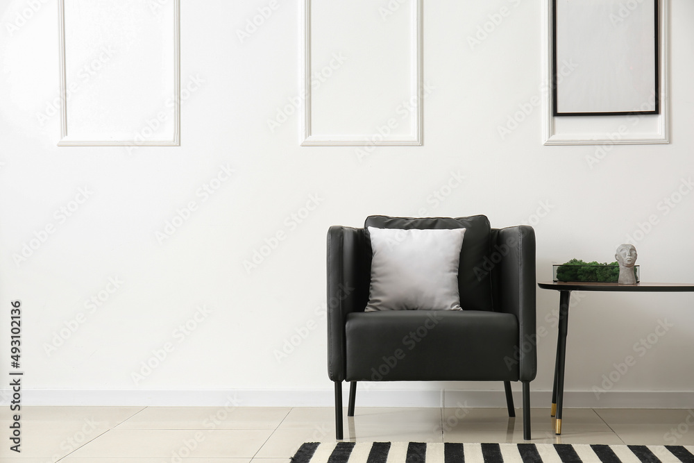 Table with decorative moss and black armchair near light wall