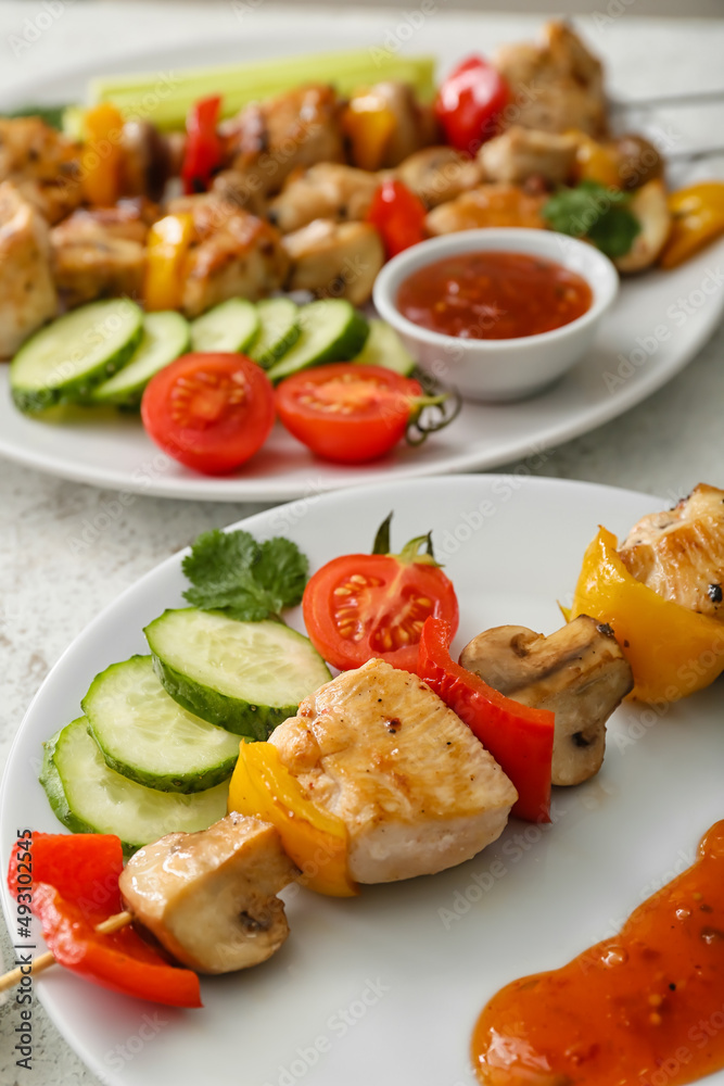 Plates of grilled chicken skewers with vegetables on table