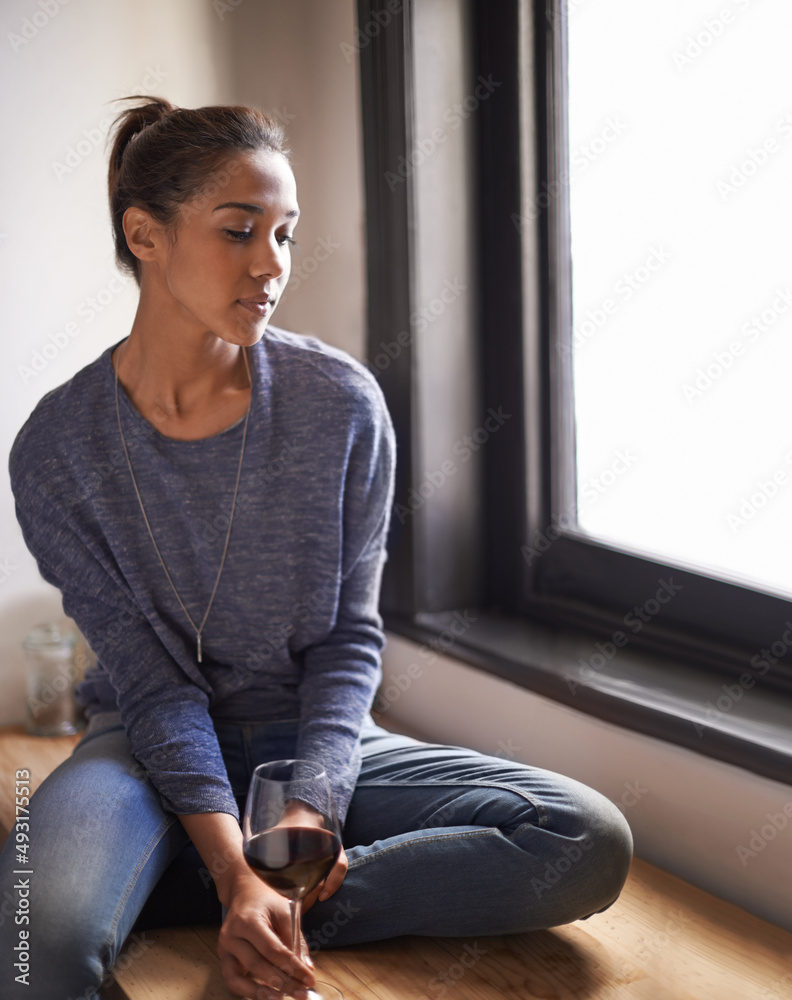 在家里喝一杯葡萄酒放松。一个年轻女人坐在窗台上喝一杯酒