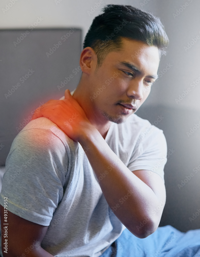 Maybe I overdid it at the gym yesterday.... Shot of a young man rubbing his sore shoulder while sitt