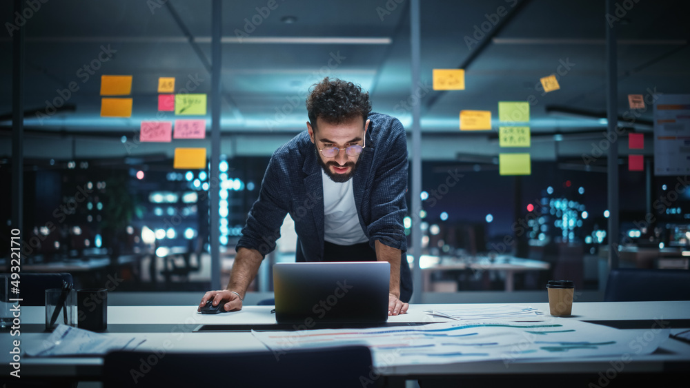 Successful Handsome Creative Director Working on Laptop Computer in Big City Office Late in the Even