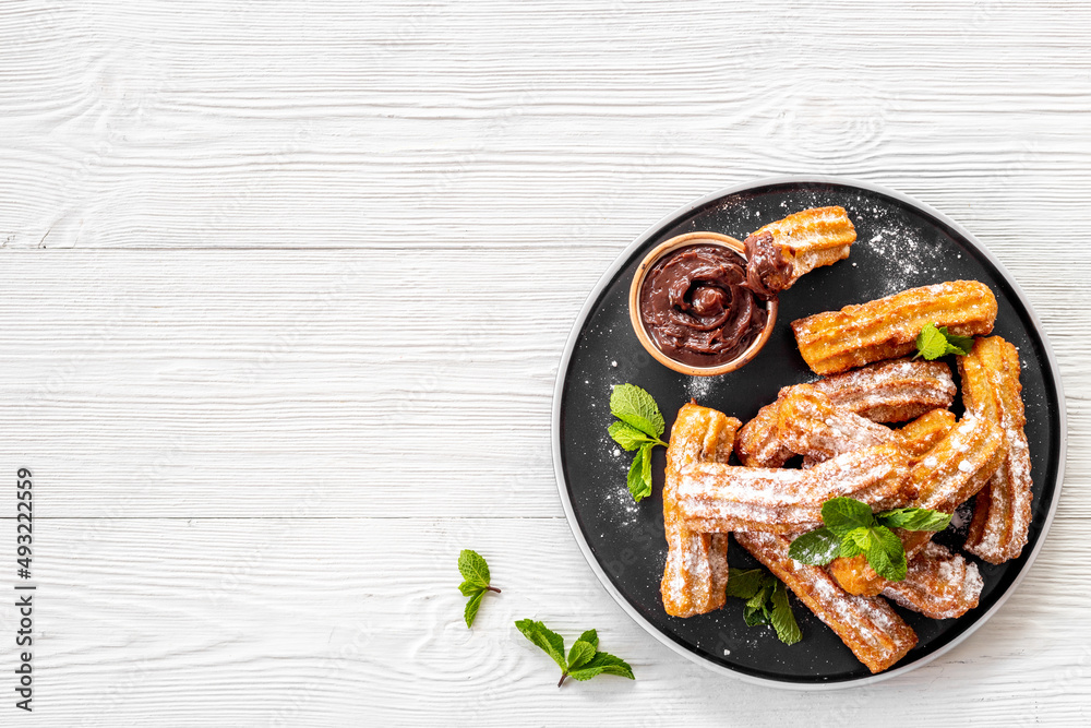 Plate with fried churros and chocolate sauce, top view