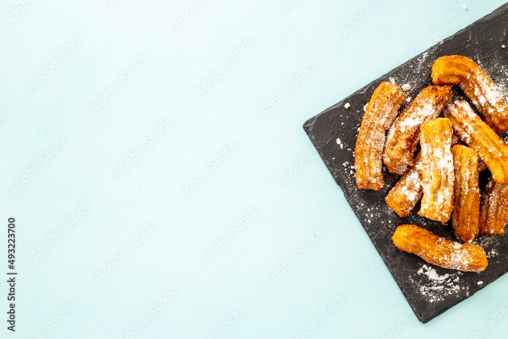 Churros with powdered sugar on black plate. Fat fast food sweets