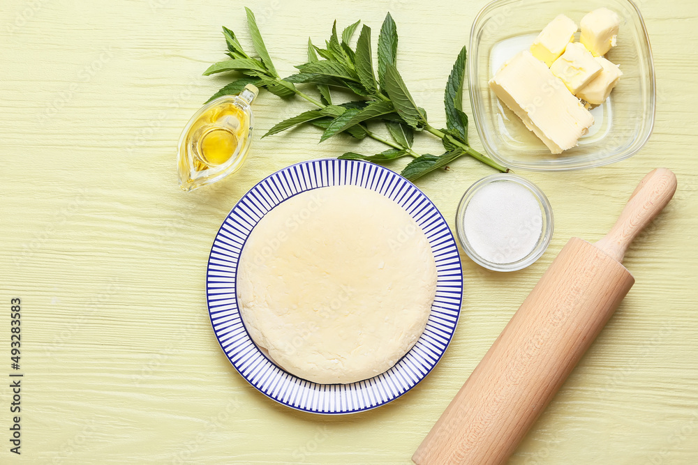 Plate with dough for preparing lazy dumplings, ingredients and rolling pin on color wooden backgroun