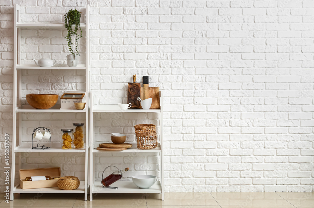 Modern shelf units with kitchenware near white brick wall