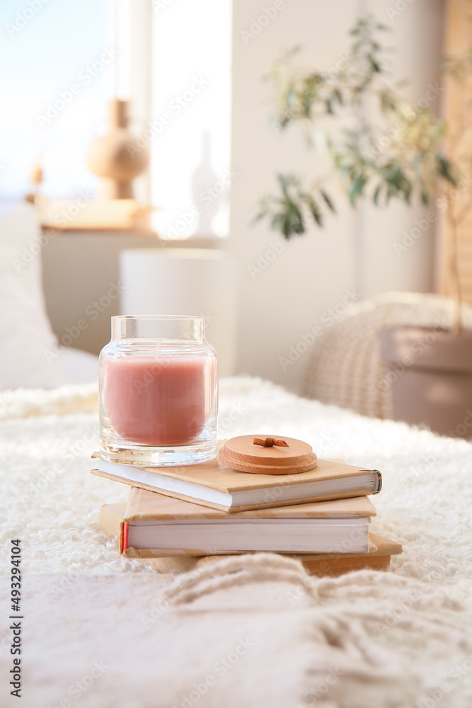 Candle with books on bed in room