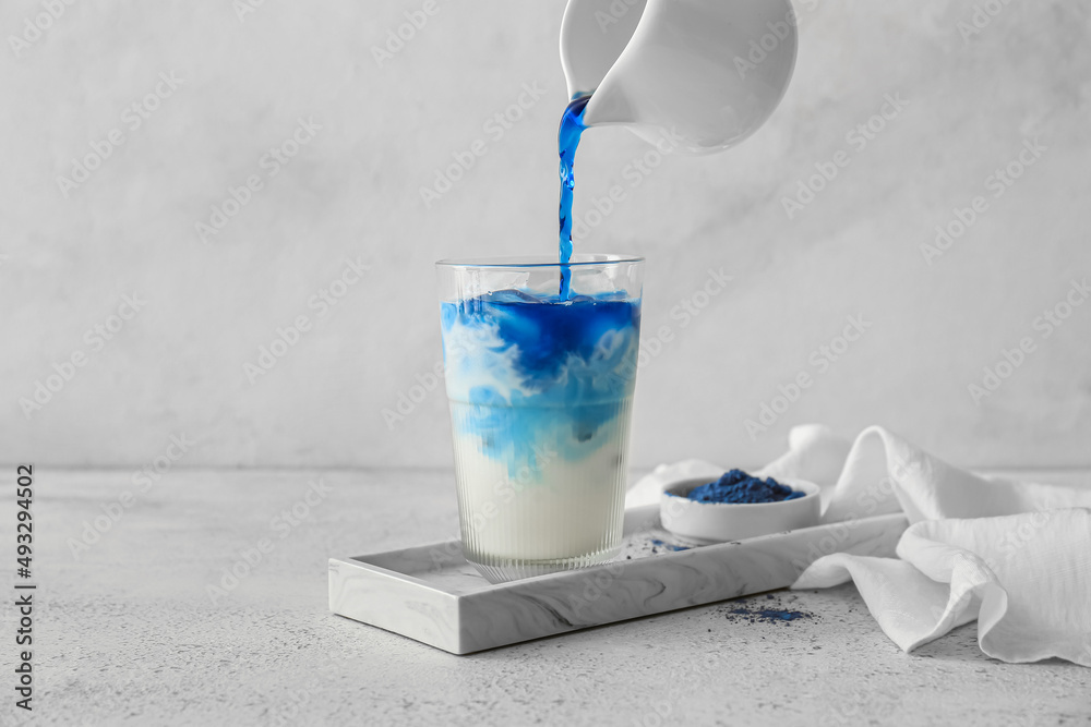 Pouring blue matcha tea in glass with milk on light background