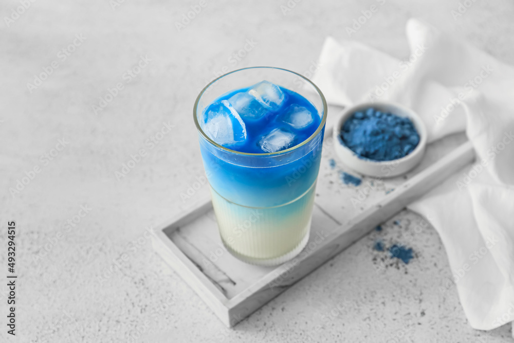 Glass of blue matcha tea and bowl with powder on light background