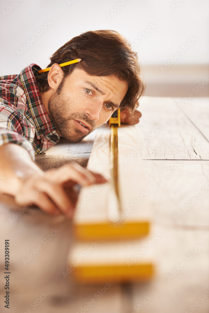 Hes a skilled carpenter. A handsome young carpenter measuring and marking wood.