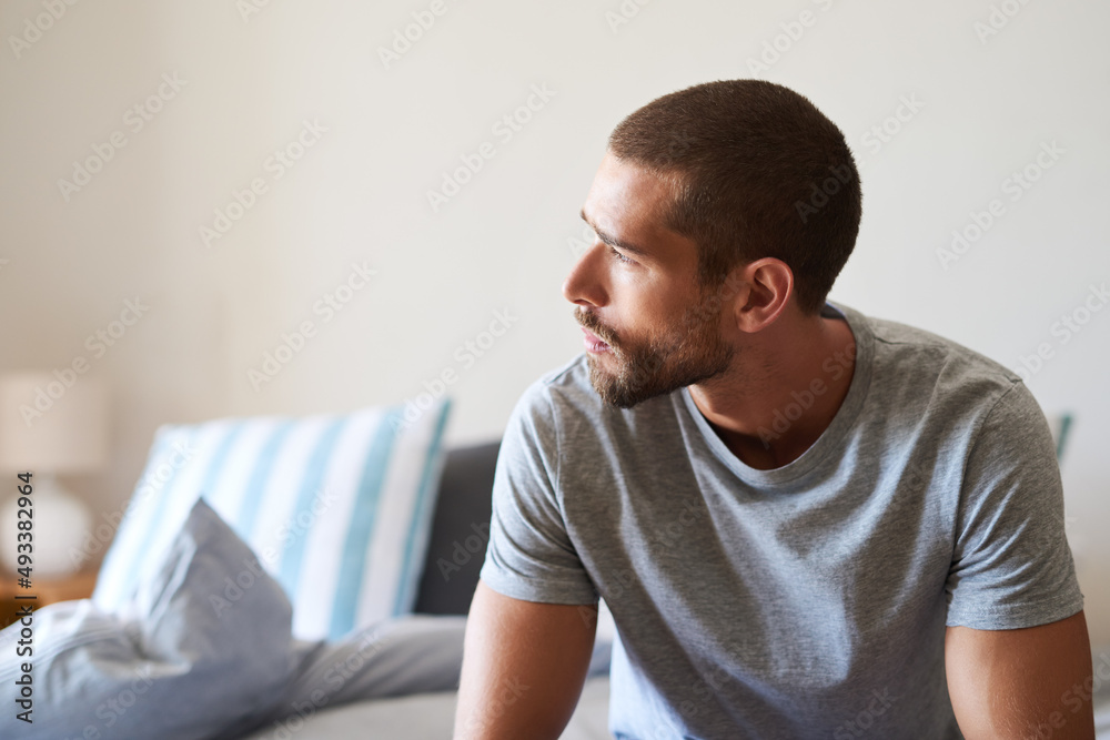 Time to rise and grind. Shot of a handsome young man looking thoughtful in his bedroom at home.