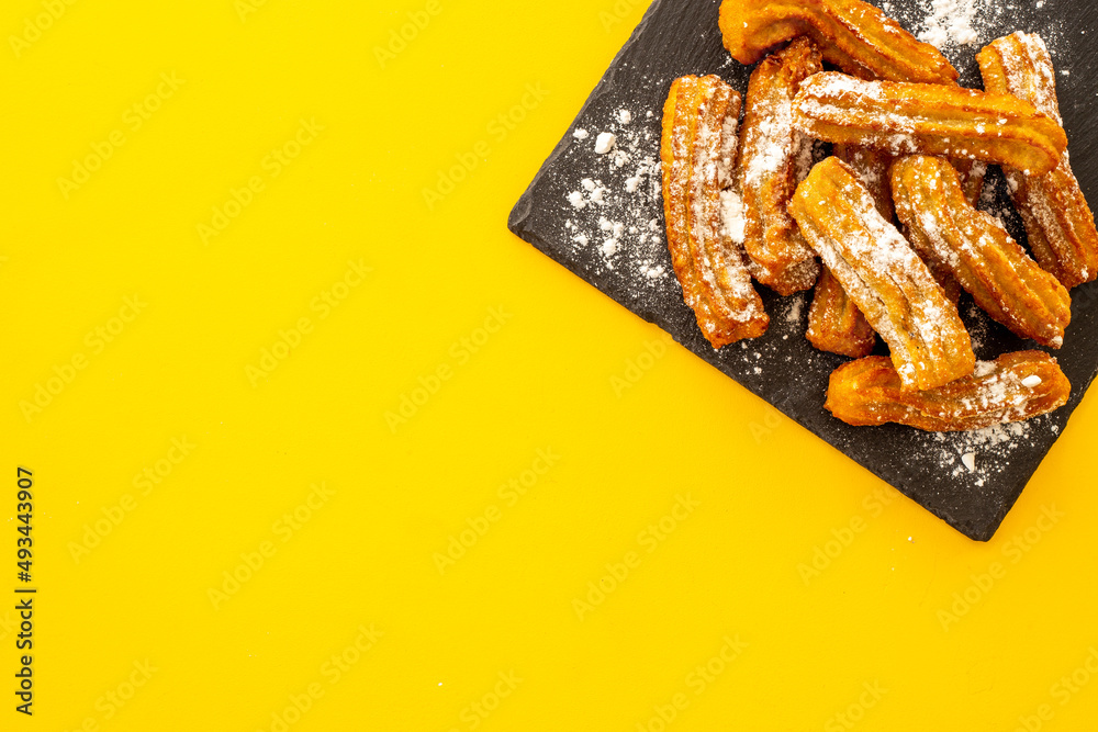 Churros with powdered sugar on black plate. Fat fast food sweets