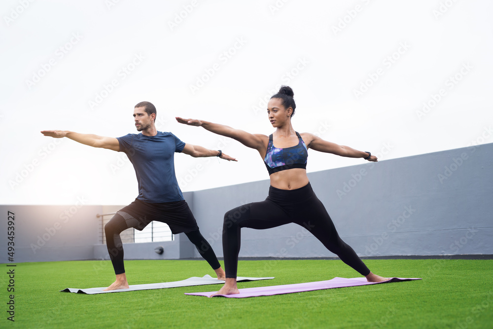 Maintaining balance and form is key. Shot of a young man and woman practising yoga together outdoors