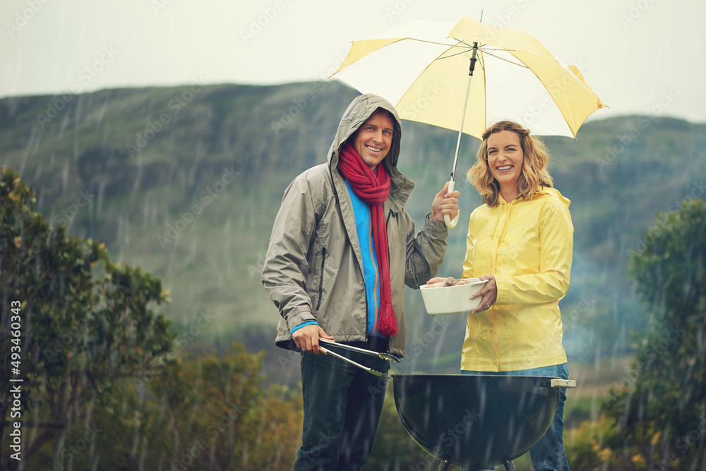 Come rain or shine. Shot of a couple happily barbecuing in the rain.