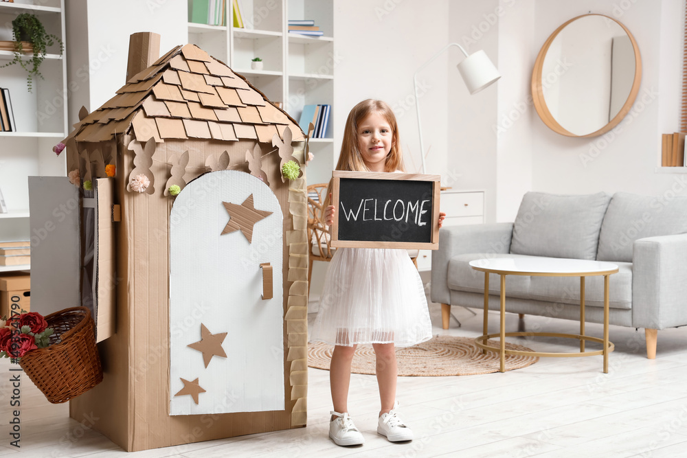 Cute little girl holding chalkboard with word WELCOME at home