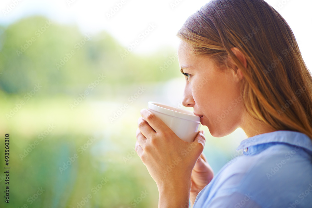 杯子里的满足感。一个年轻女人站在窗户边喝咖啡的裁剪镜头。