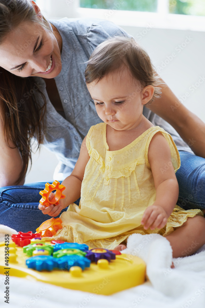 Teaching her little one. Shot of a cute baby girl sitting on the floor with her mom and playing with