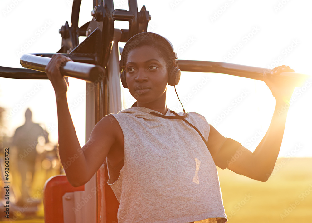 Staying fit and strong. A young woman using outdoor exercise equipment at the park.