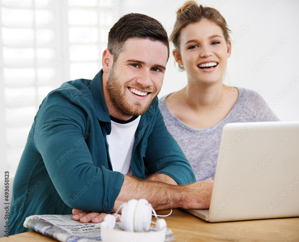 Were one connected couple. Portrait of a smiling young couple using a laptop while relaxing at home 