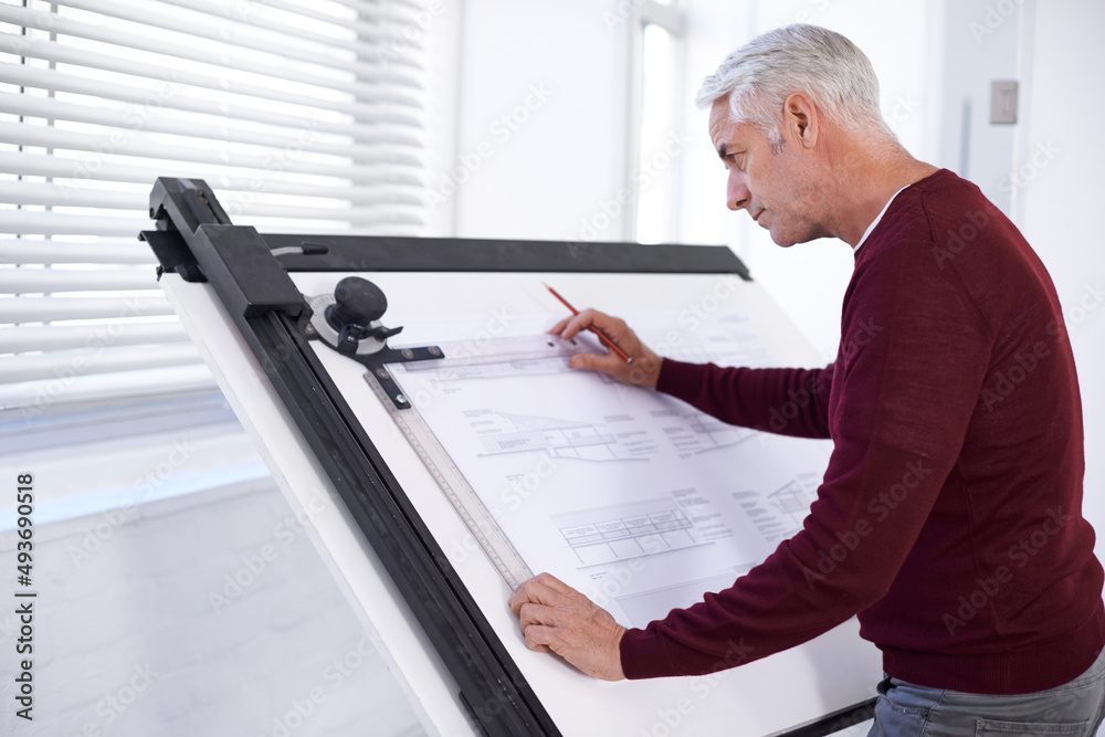 Doing what he does best. Cropped shot of a male architect working on a building plan at a drawing bo