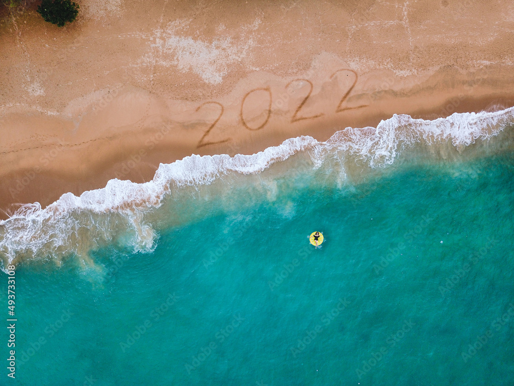 Happy New Year 2022, lettering on the beach with wave and blue sea. Numbers 2022 year on the sea sho