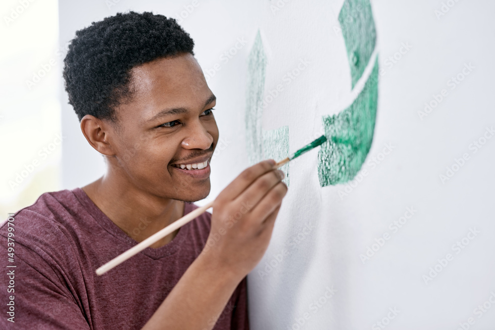 The green life is the good life. Shot of a young man painting a recycle symbol on a wall.