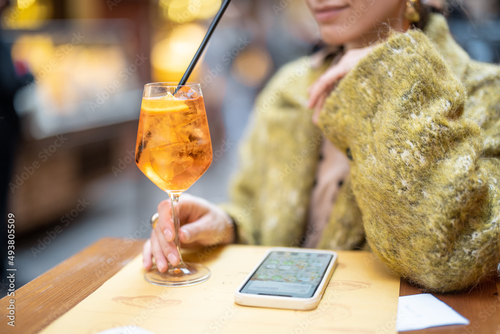 女人在户外酒吧拿着装有Aperol Spritz鸡尾酒的杯子，短镜头聚焦于饮料