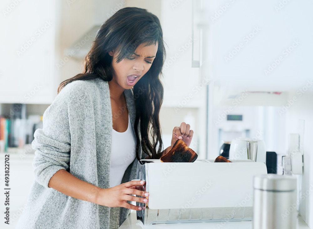 I cant eat this. Shot of a shocked young woman removing burnt toast from her toaster.