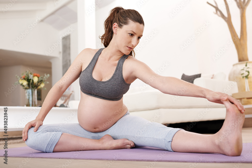 Stretching before exercise. Shot of a young pregnant woman exercising at home.