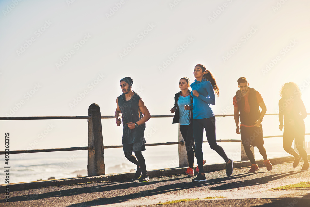 Working hard to conquer that inner couch potato. Shot of a fitness group out running on the promenad