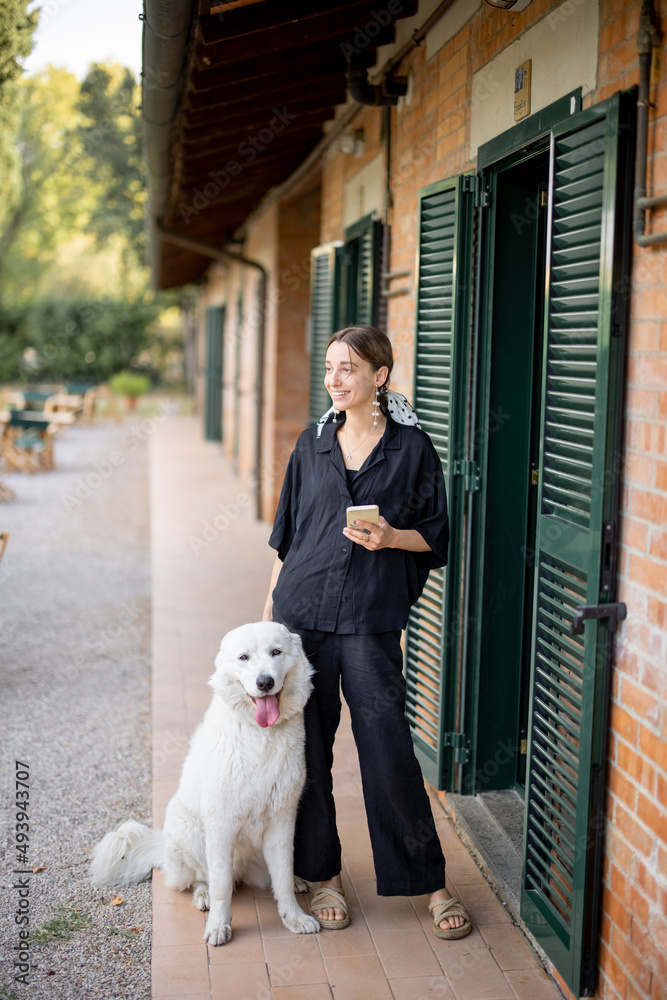 年轻的高加索女性与Maremmano Abruzzese Sheepdog站在一起，在h入口附近向外看