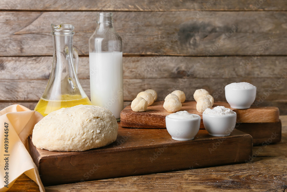 Boards with dough, raw lazy dumplings and ingredients on wooden background