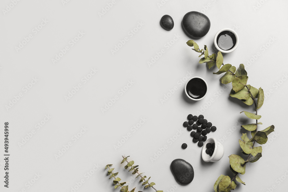 Composition with bowls of activated carbon mask, pills and eucalyptus branch on white background