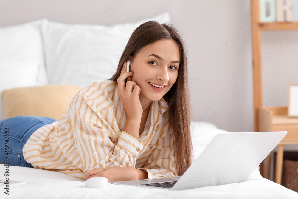 Pretty young woman with laptop listening to music in bedroom