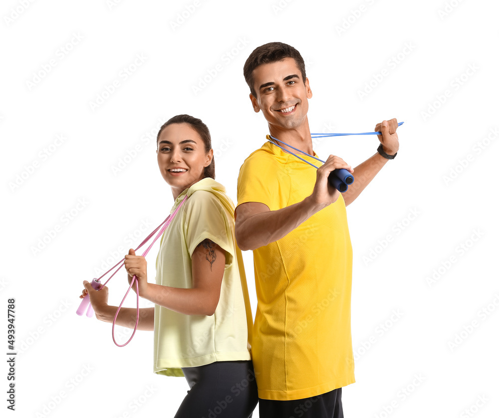 Sporty young couple with jumping ropes on white background