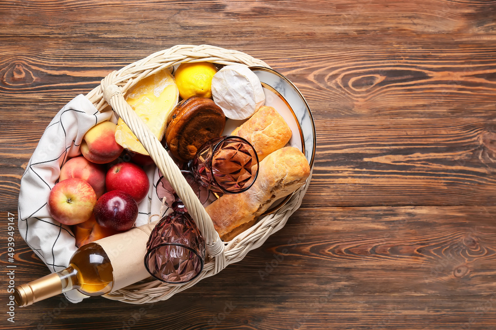 Wicker basket with tasty food and wine for picnic on wooden background