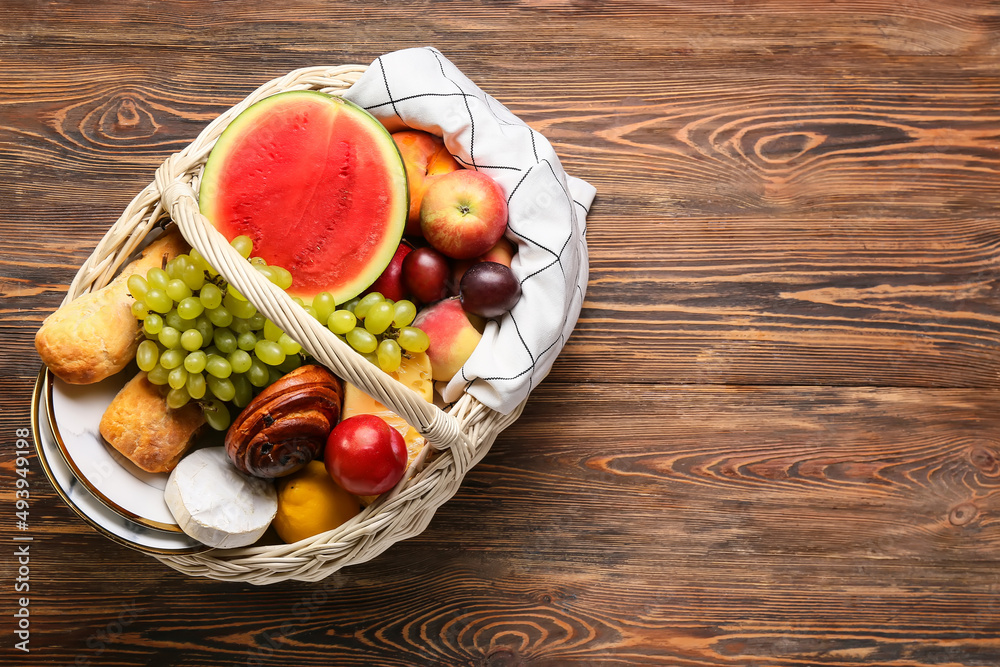 Wicker basket with tasty food for picnic on wooden background