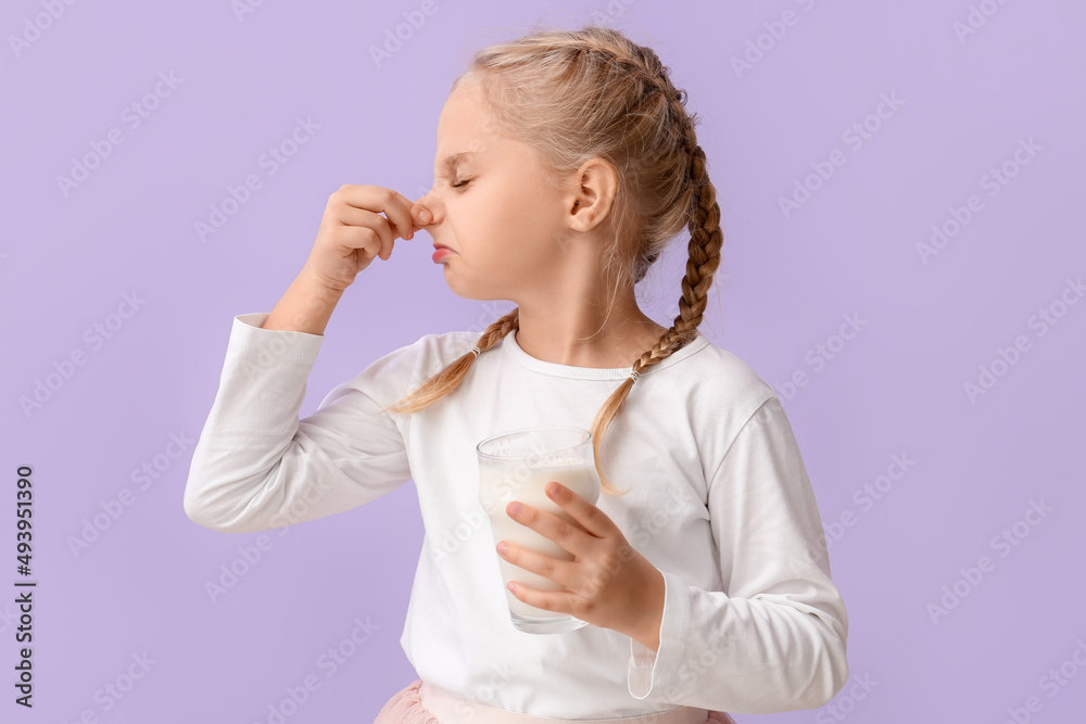 Cute little girl with glass of milk closing nose on lilac background