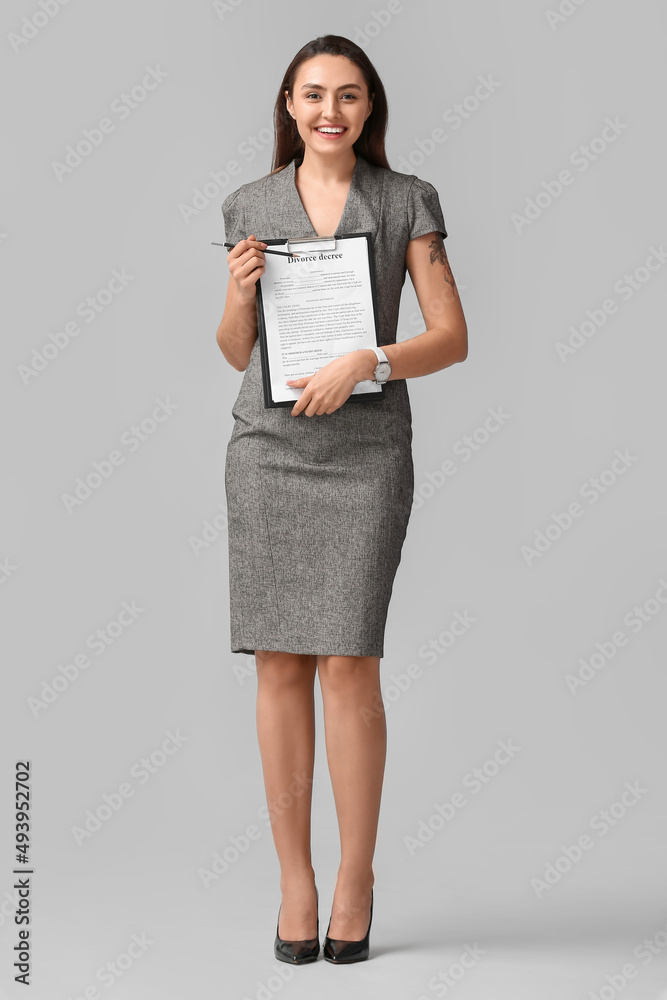 Pretty young businesswoman with clipboard on light background