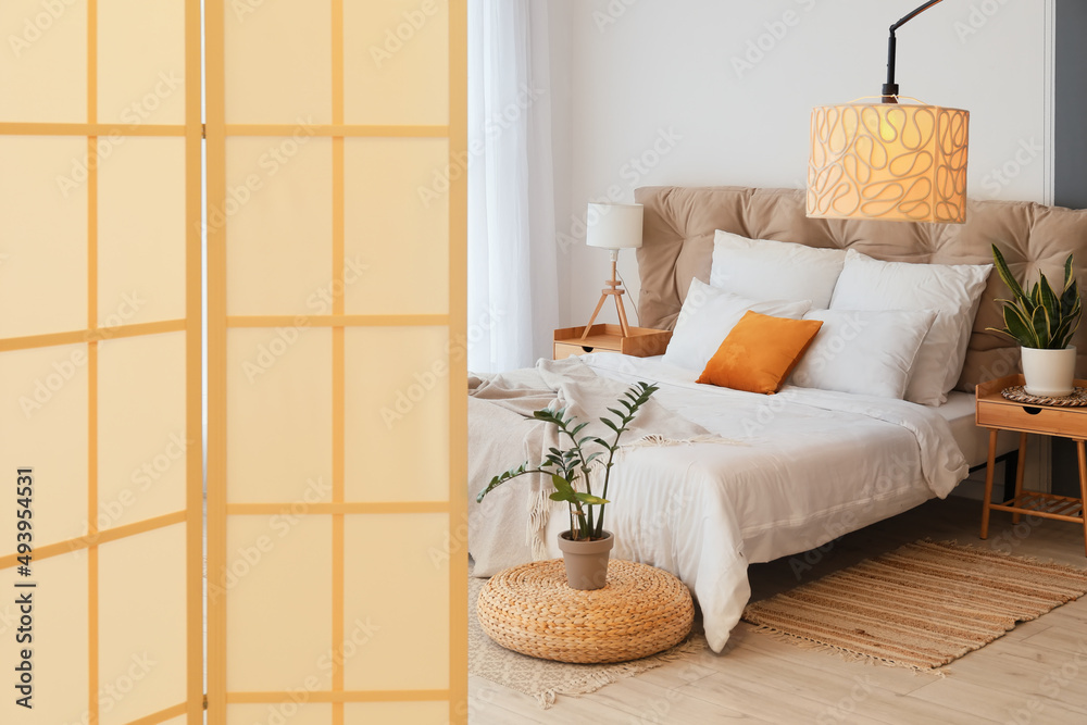 Interior of modern bedroom with stylish folding screen and houseplants