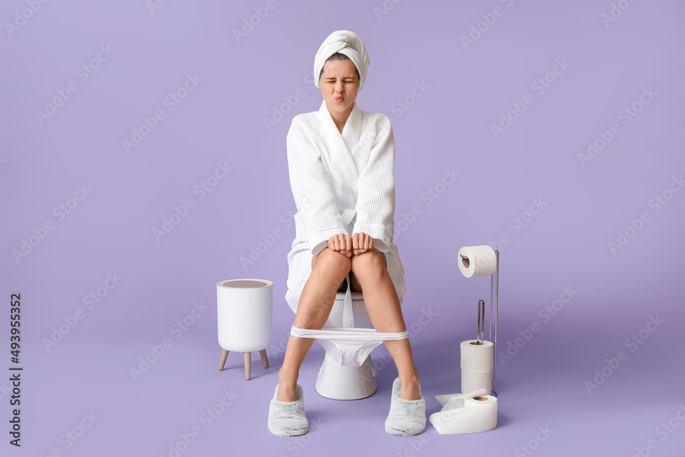 Young woman suffering from diarrhea while sitting on toilet bowl against color background