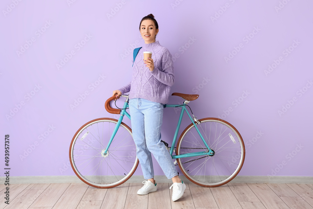 Portrait of beautiful female student with cup of coffee and bicycle near color wall