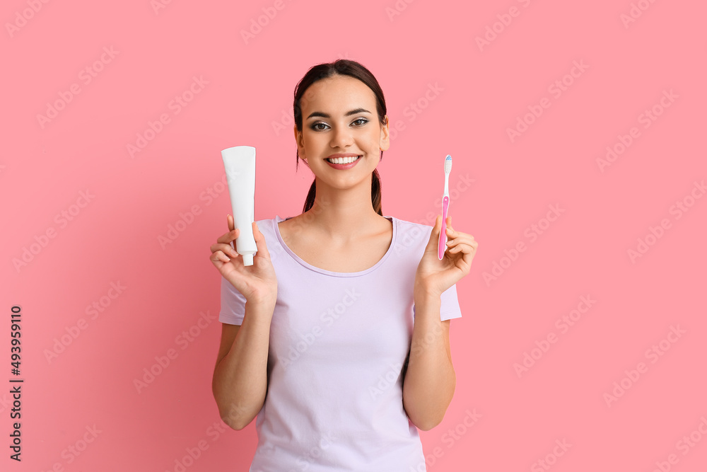 Smiling young woman with tooth paste and brush on pink background