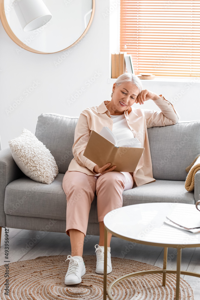 Mature woman reading book while sitting on sofa