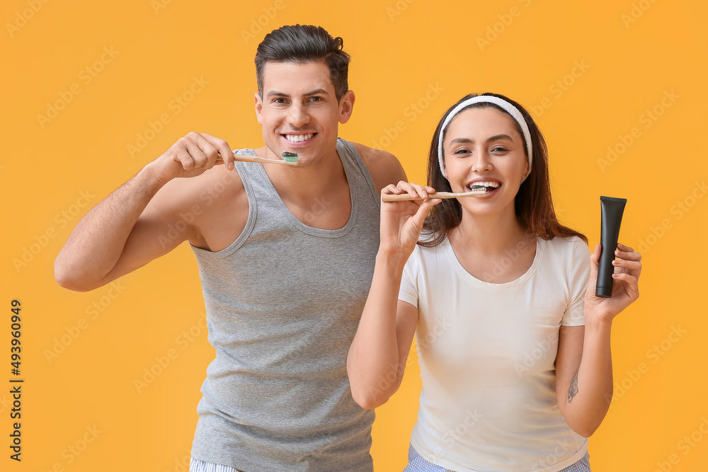 Young couple brushing teeth with activated charcoal tooth paste on yellow background